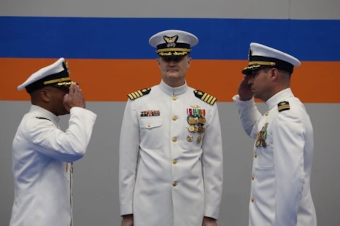 The incoming and outgoing Coast Guard commanding officers salute each other in front of the ceremony’s presiding officer.