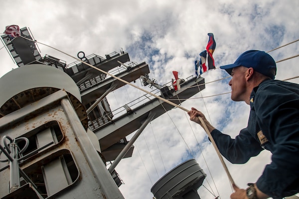 Navy Quartermaster Senior Chief Benjamin Richards shifts colors on the mast of Nimitz-class aircraft USS Nimitz (CVN 68) after pulling pierside at Naval Station Mayport in Jacksonville, Florida, June 16, 2026. Nimitz is underway in the U.S. 2nd Fleet area of operations as part of a scheduled homeport shift to Norfolk, Virginia.  (U.S. Navy photo by Mass Communication Specialist 2nd Class Jaron Wills)