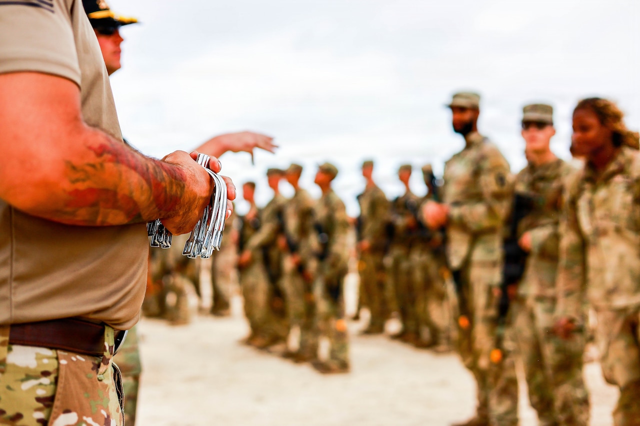A soldier holds a batch of spurs while another talks to a group of soldiers who are out of focus.