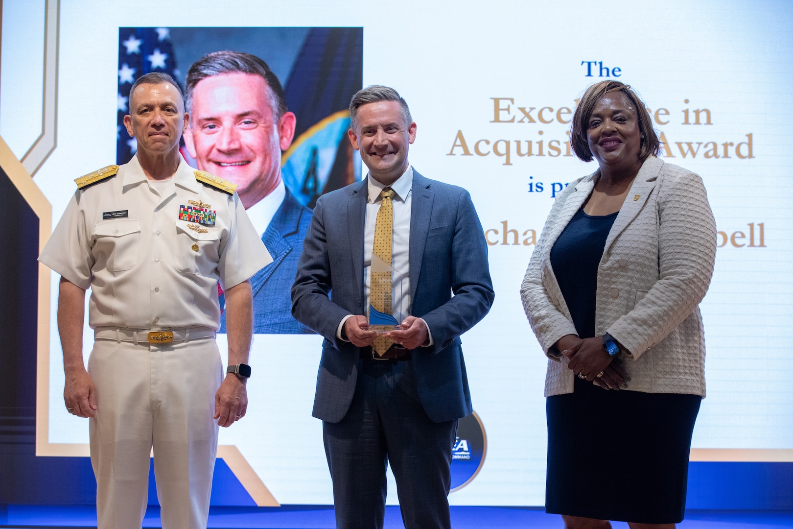WASHINGTON, DC (June 11, 2026) - Vice Admiral Jim Downey, Commander, Naval Sea Systems Command (NAVSEA) and Ms. Leslie Joseph, Deputy Commander, Total Force and Corporate Operations, hosted the NAVSEA Excellence Awards in the auditorium. The 2025 NAVSEA Excellence in Acquisition Award is presented to Mr. Michael J. Campbell (center).