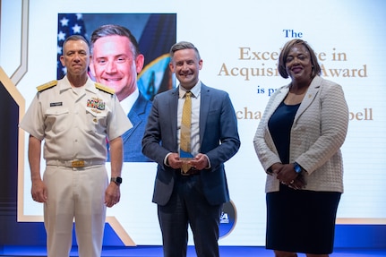WASHINGTON, DC (June 11, 2026) - Vice Admiral Jim Downey, Commander, Naval Sea Systems Command (NAVSEA) and Ms. Leslie Joseph, Deputy Commander, Total Force and Corporate Operations, hosted the NAVSEA Excellence Awards in the auditorium. The 2025 NAVSEA Excellence in Acquisition Award is presented to Mr. Michael J. Campbell (center).