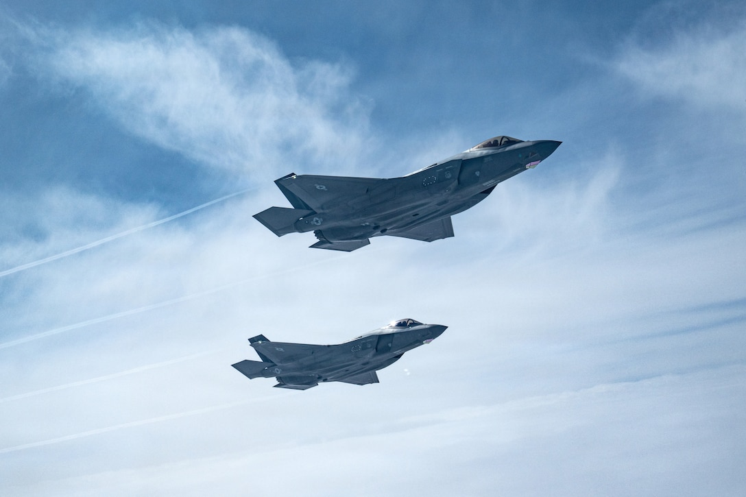 Two fighter jet aircraft fly near each other in the same direction against a partially cloudy sky.