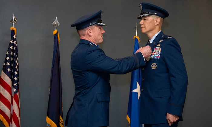 A man in uniform pins a medal to the lapel of another man in uniform.