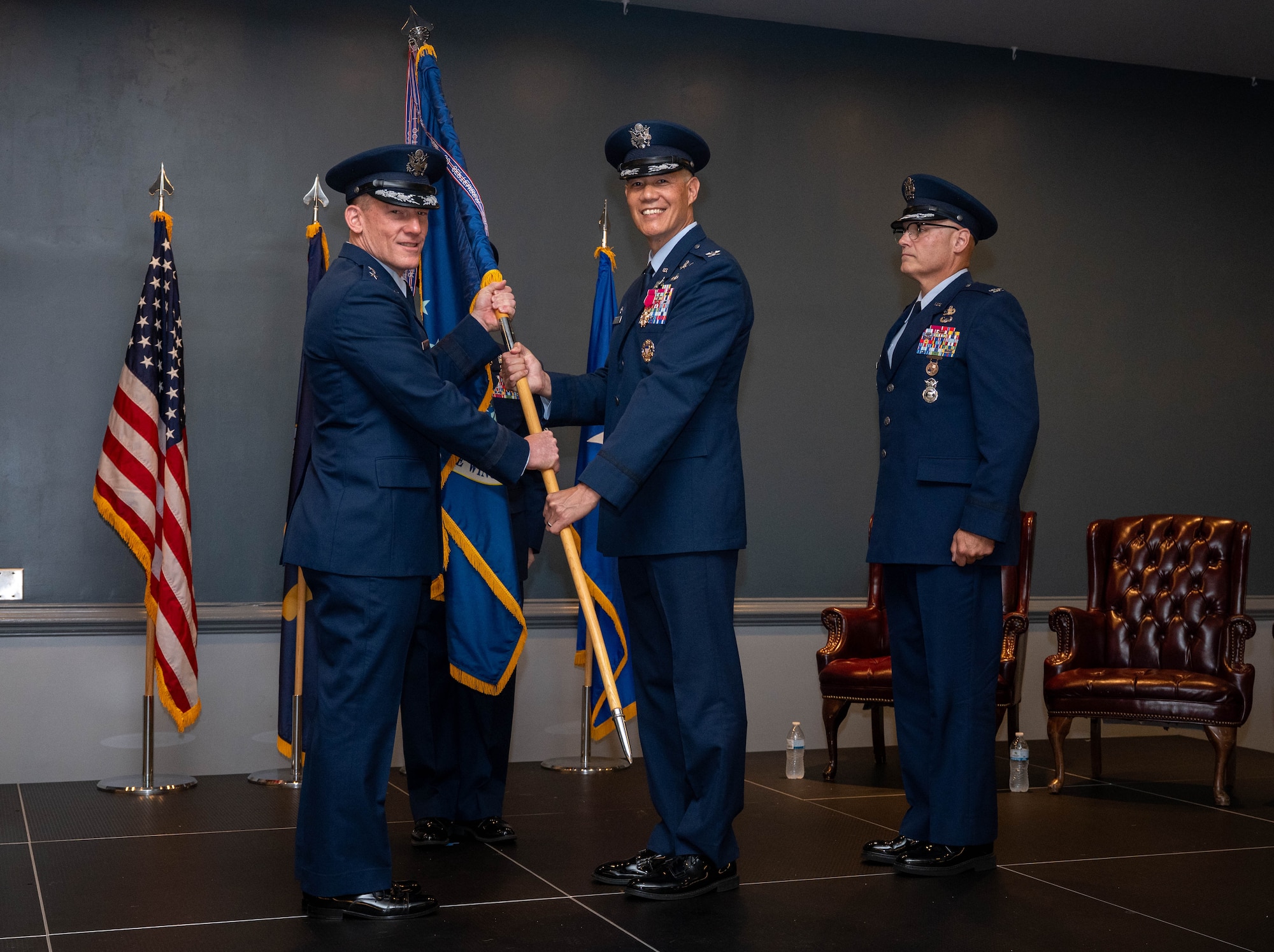 Four men in uniform stand on a stage, two holding a flag and two standing at attention.