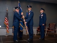 Four men in uniform stand on a stage, two holding a flag and two standing at attention.