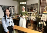 two women, one in colonial clothing, stand in front of colonial display