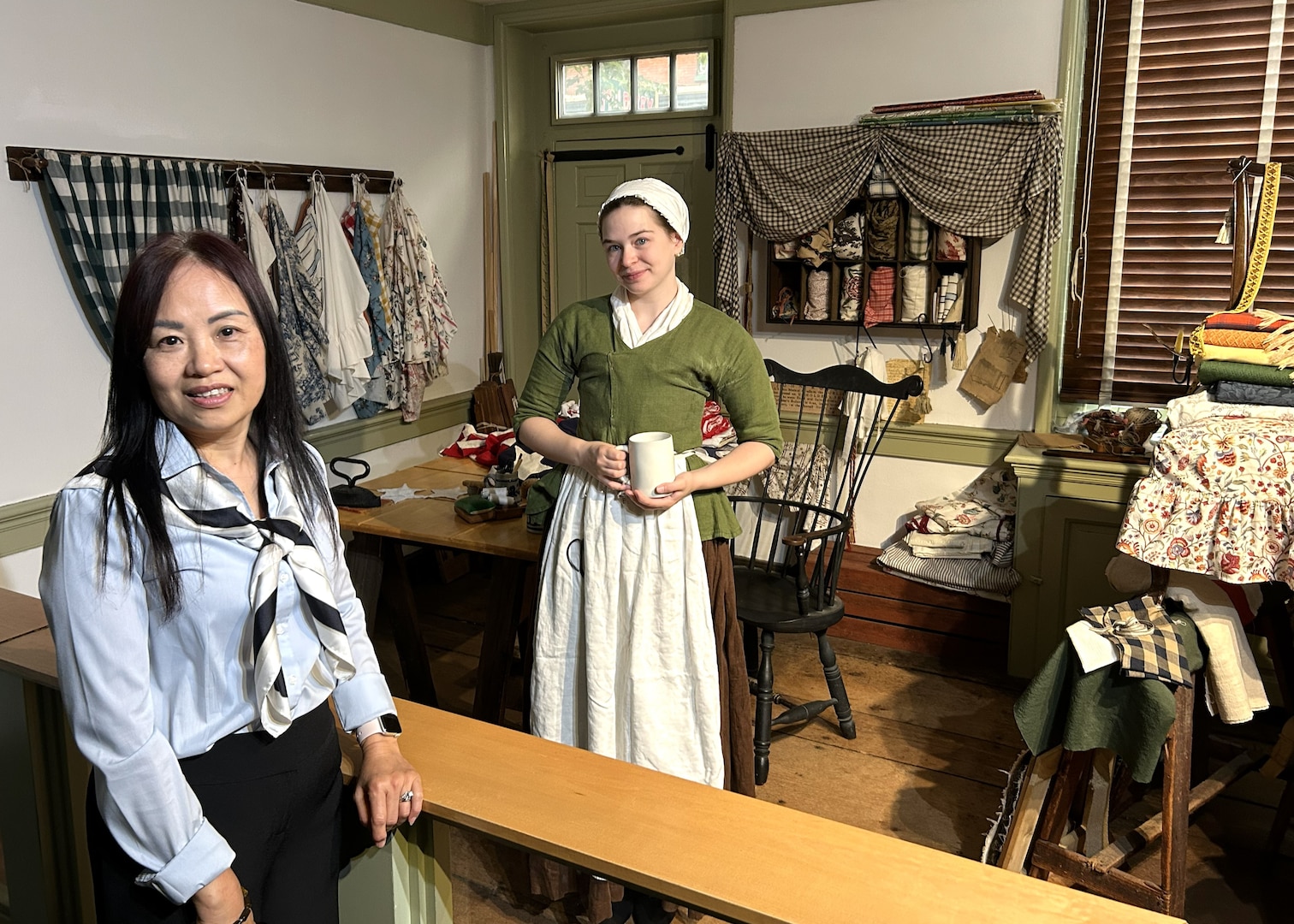 two women, one in colonial clothing, stand in front of colonial display