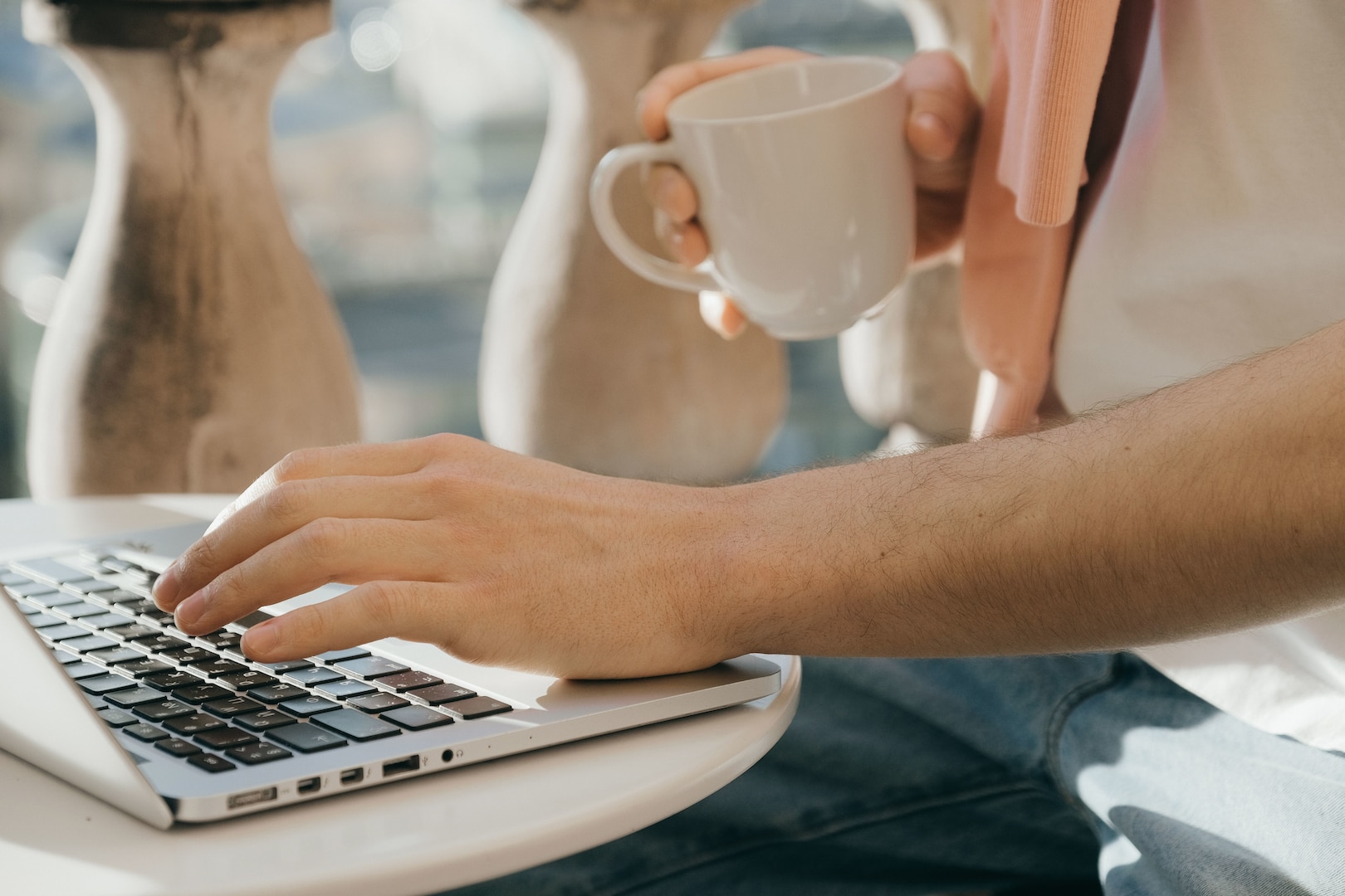 A person typing on a laptop with their left hand while holding a mug in their right hand.