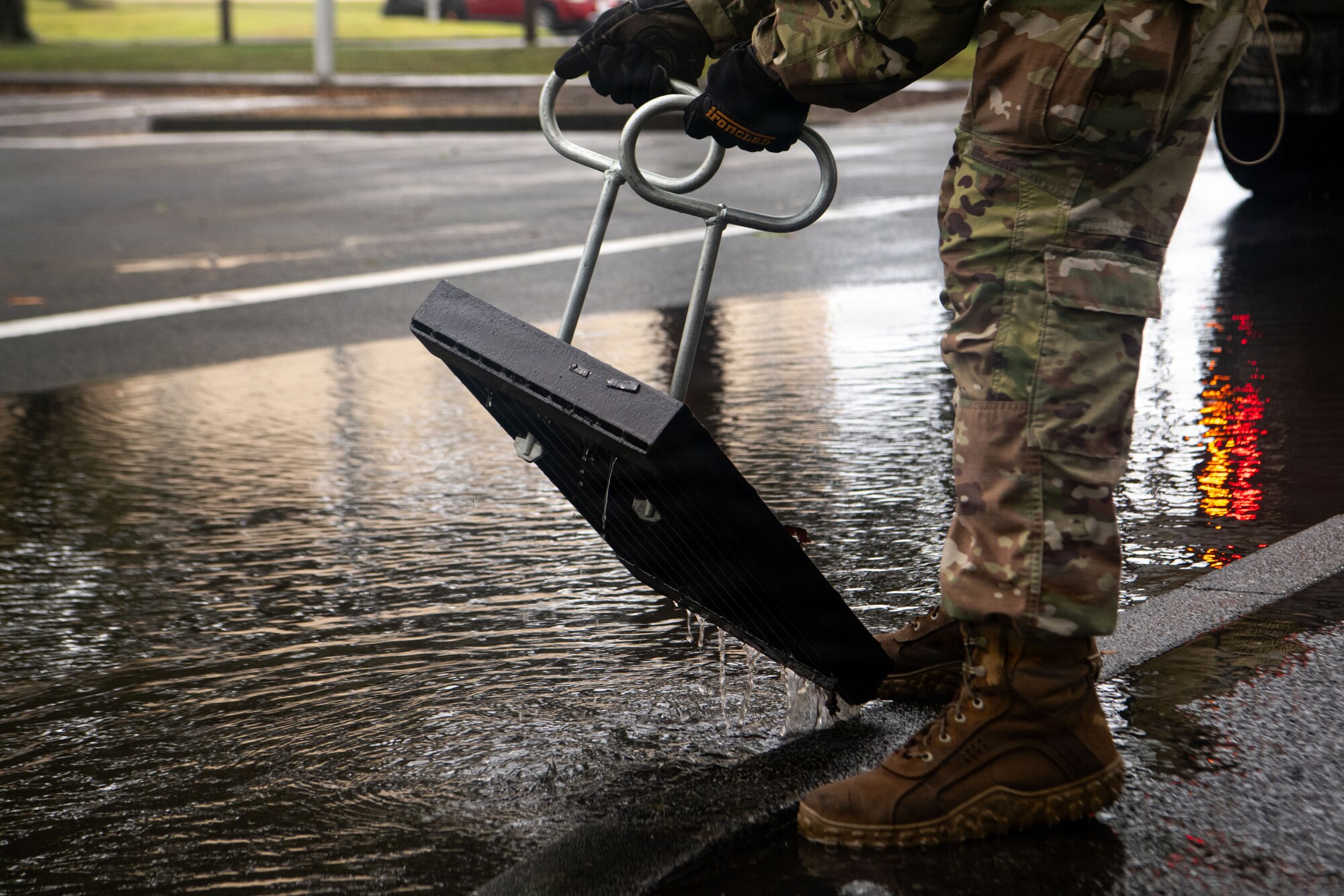 An Airman lifts a cover to unclog a storm drain.