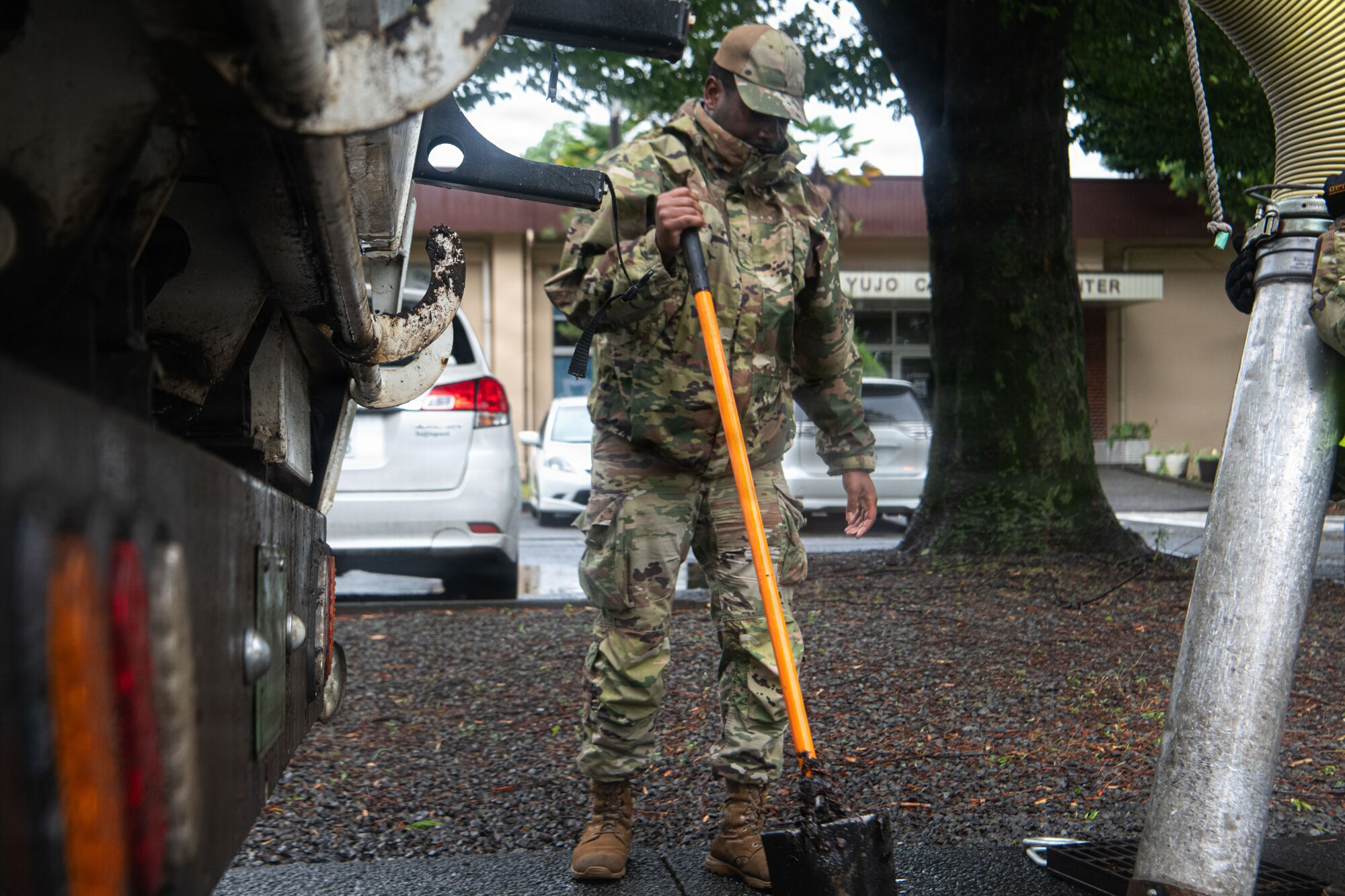 Tech. Sgt. Carter using a shovel to break up debris and vacuuming water out of a clogged storm drain.