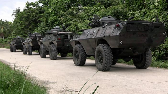 The ASV, 4-wheeled armored vehicles from a rear angle, sit in a line on a dirt road.