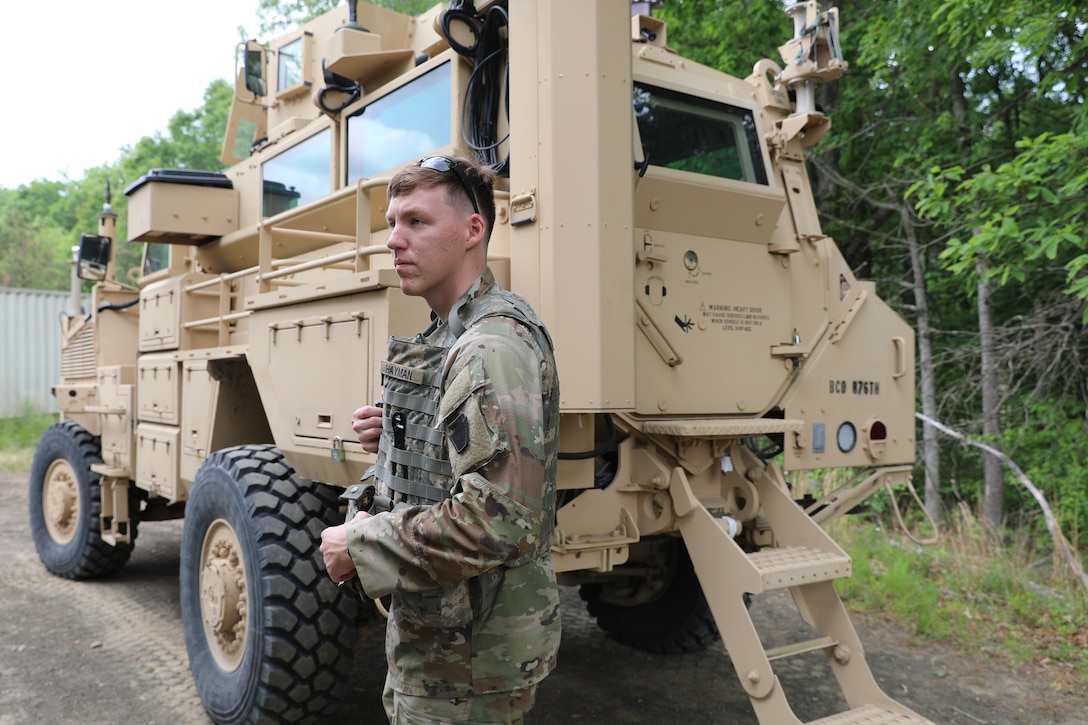 A uniformed man stands in front of a tan vehicle.