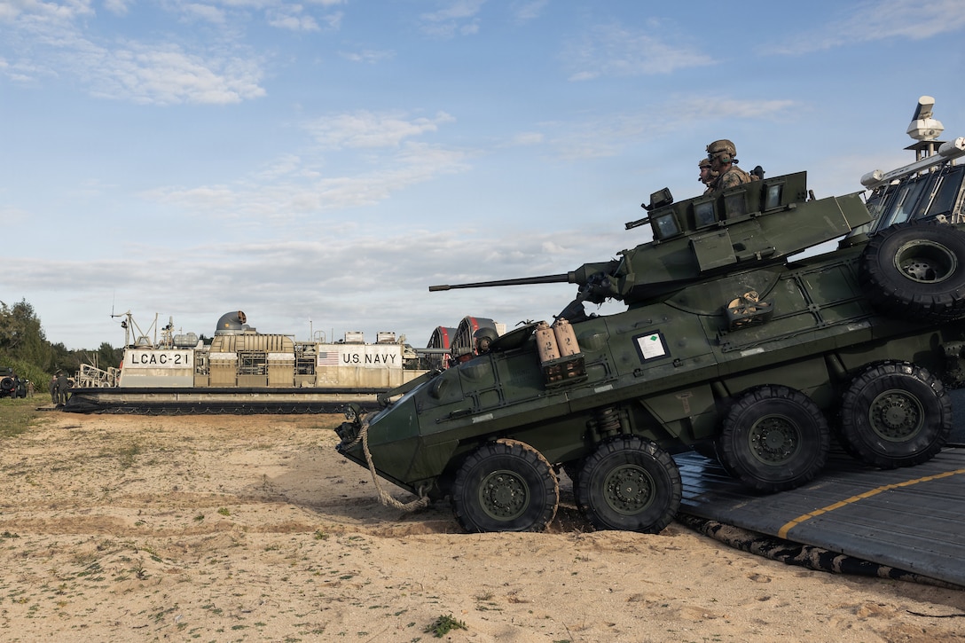A wheeled vehicle with a tank profile rolls off a ship ramp.