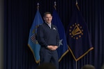 An Air Force major general stands on a stage with military flags behind him.