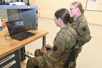Sgt. Sophia Staskowski, left, uses a drone simulator, while Sgt. Syerra Freeman watches June 10, 2026, at the Unmanned Aircraft System Training and Innovation Facility at Fort Indiantown Gap, Pennsylvania. Both Soldiers are members of Mike Company, 56th Mobile Brigade Combat Team and work full-time at the UAS TIF. (Pennsylvania National Guard photo by Brad Rhen)