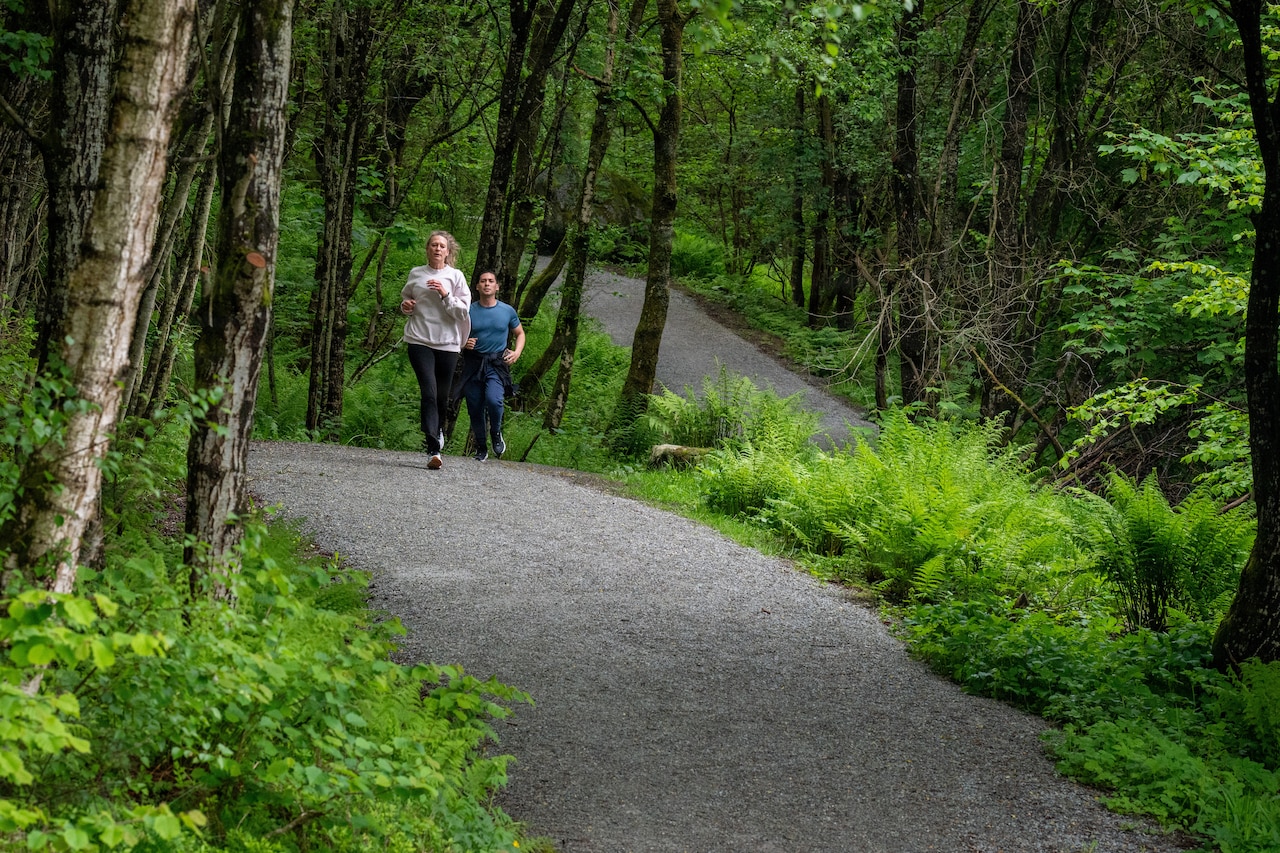 A woman and a man in athletic attire run down a path in a forest.