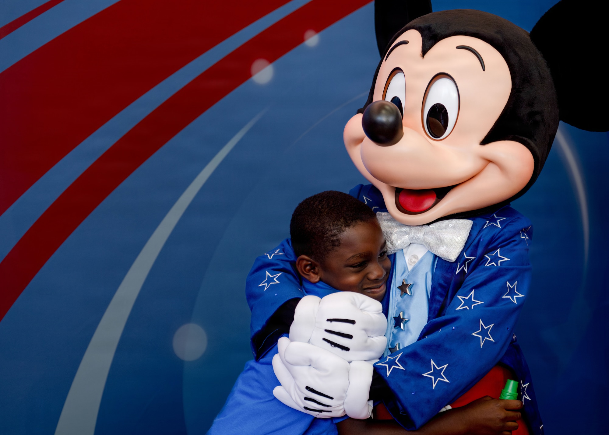 Mickey Mouse hugs a military child during a Blue Star Families event at MacDill Air Force Base, Florida, June 16, 2026. The Second Lady of the United States,Usha Vance, attended the event to read a children’s book to children of military members. During the event, approximately 125 children received Disney books and met Mickey Mouse along with other surprises. (U.S. Air Force photo by Airman 1st Class Nelvis Sera)