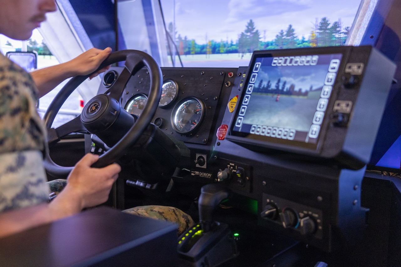 A man wearing a military camouflage uniform looks at a screen while operating a driving simulator.