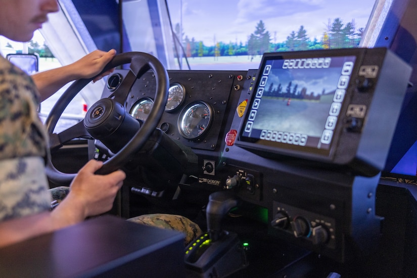 A man wearing a military camouflage uniform looks at a screen while operating a driving simulator.
