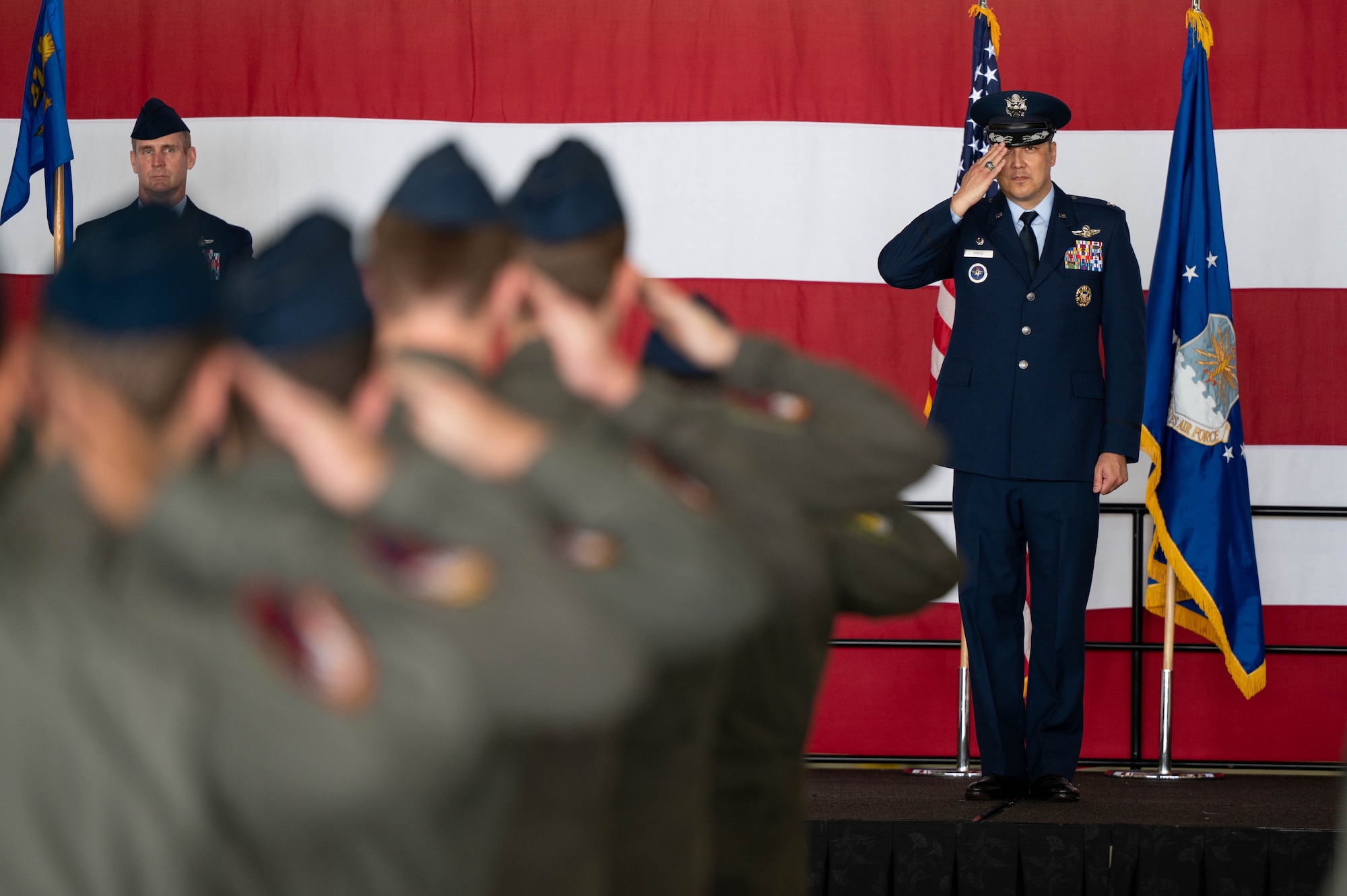 Airmen in flight suits render a salute to an Airman in service dress on a stage.