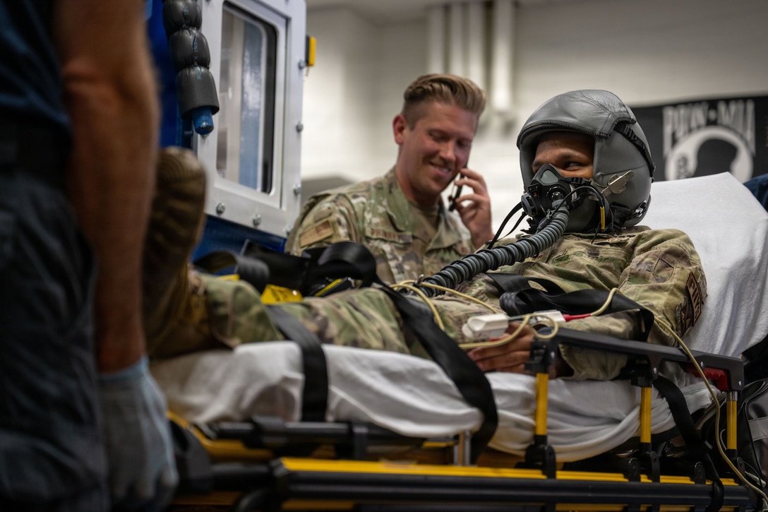 A man with a helmet and mask lays on a transportable ambulance bed.