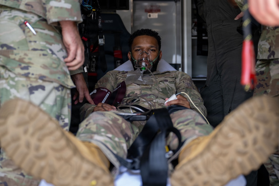 A male airman lies on a transportable bed inside an ambulance.