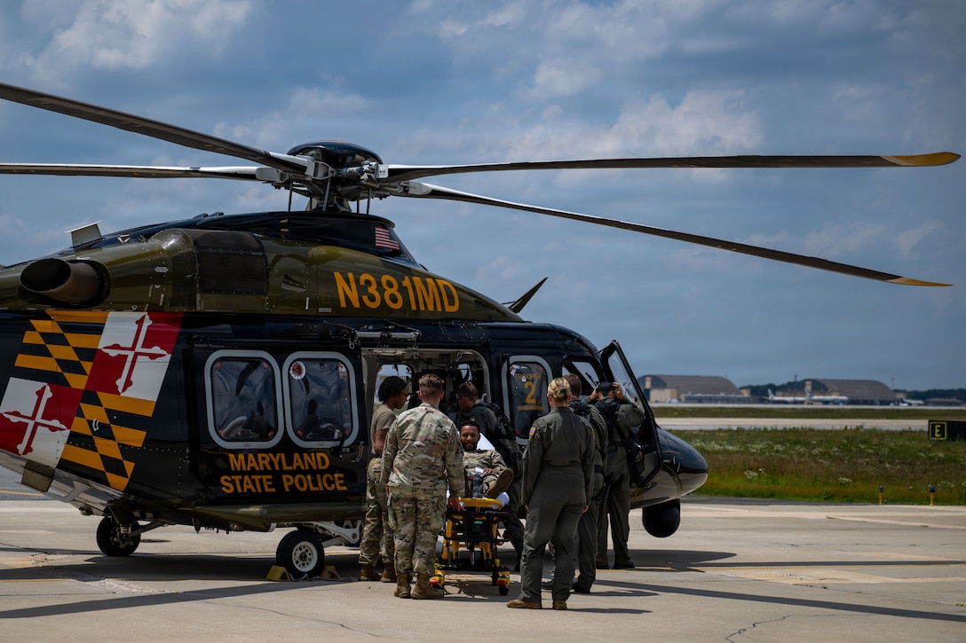 Airmen loads a simulated patient onto a helicopter that is sitting outside on a concrete flight pad.