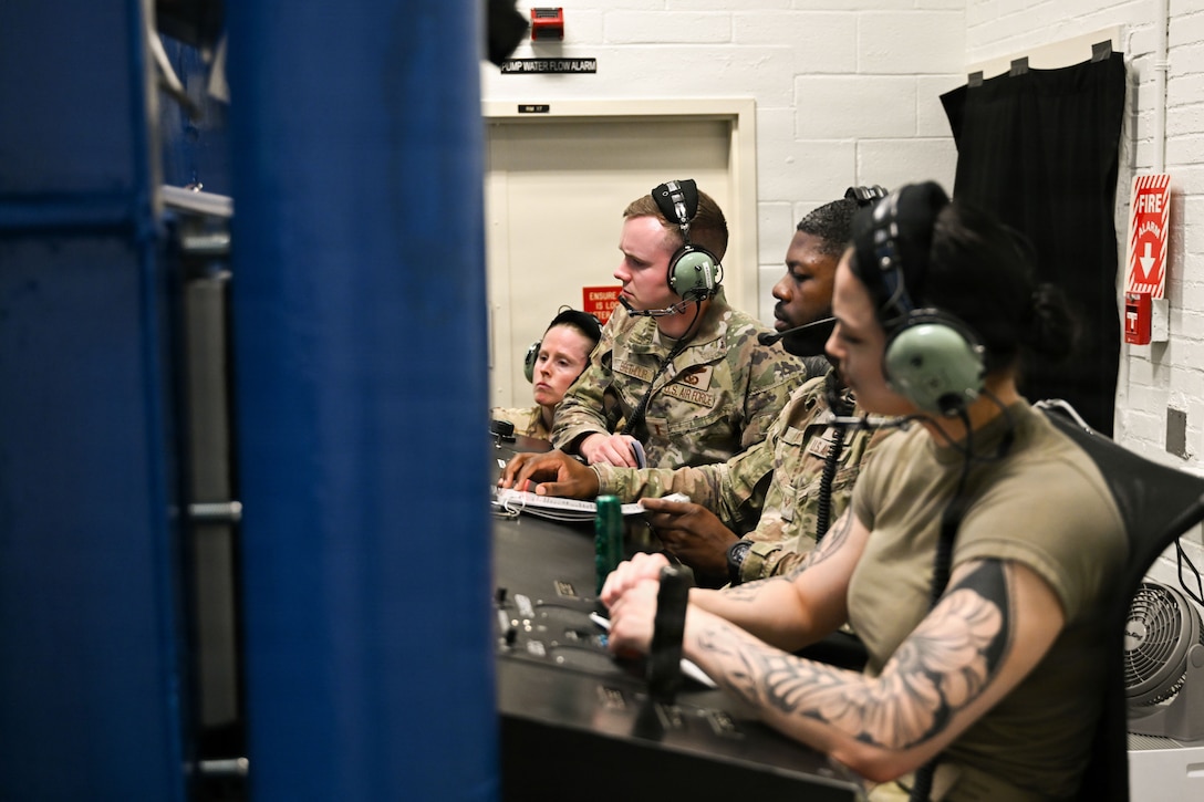 Four Airman site outside a decompression chamber at the control panel and observe the participants inside the chamber.