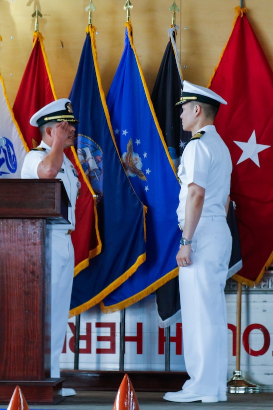 People wearing military uniforms stand on stage saluting each other