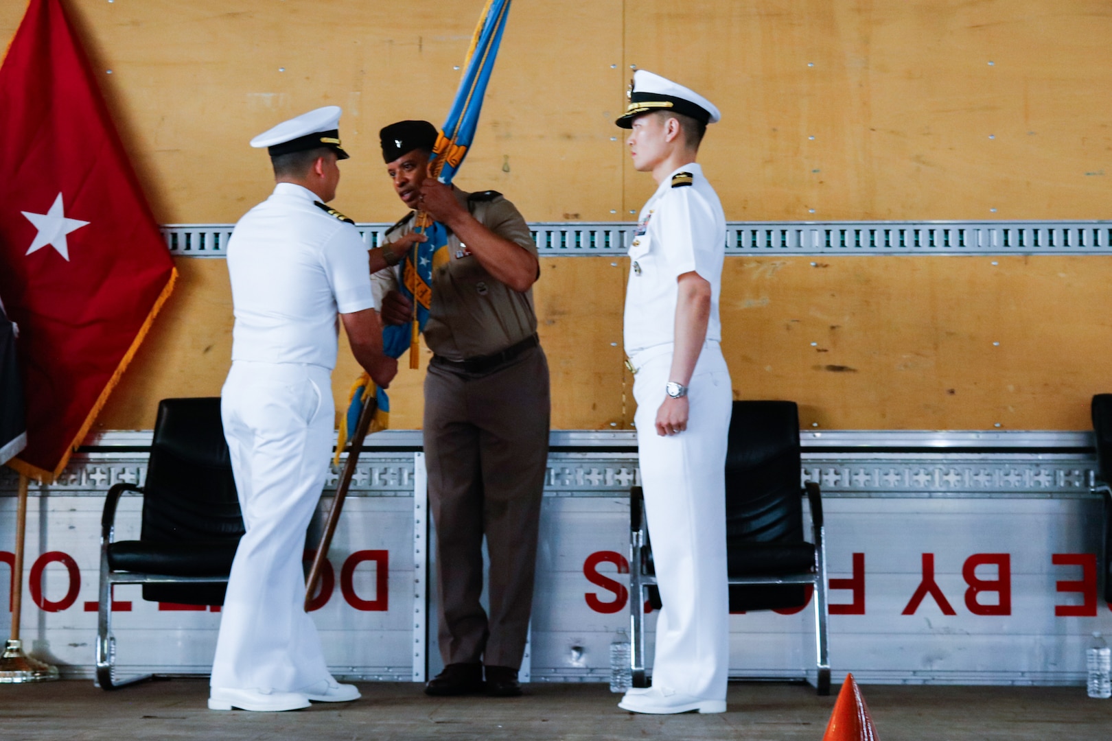 People wearing military uniforms stand on stage holding a flag