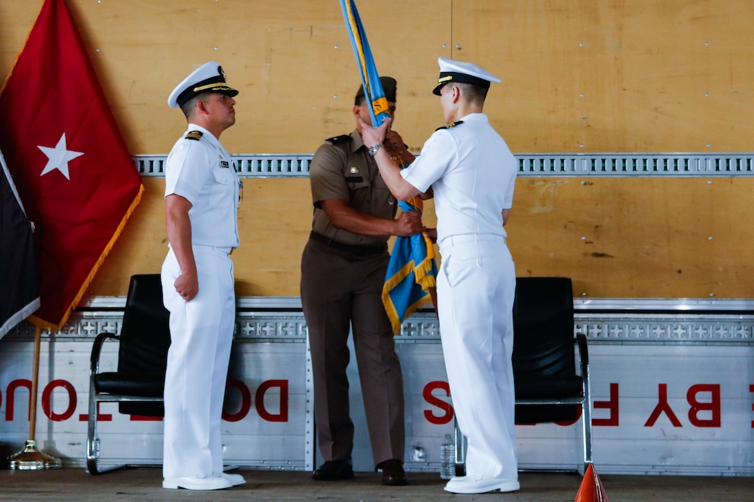 People wearing military uniforms stand on stage holding a flag