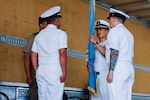 People wearing military uniforms stand on stage holding a flag