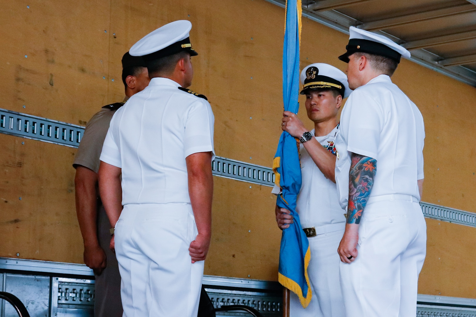 People wearing military uniforms stand on stage holding a flag