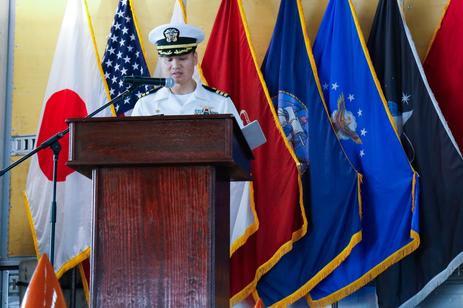 A man wearing a military uniform stands on stage behind a podium speaking.
