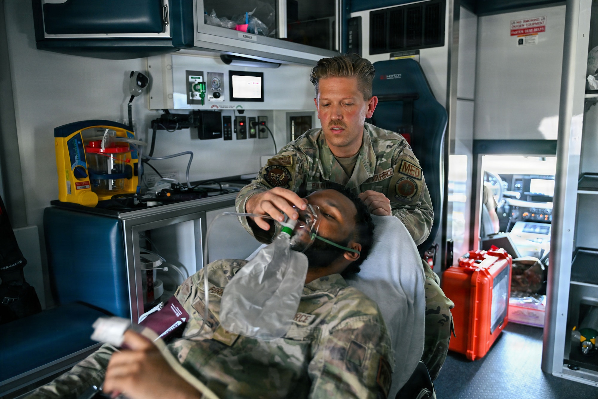 A man lies inside an ambulance. And Air Force medic adjusts his oxygen mask.
