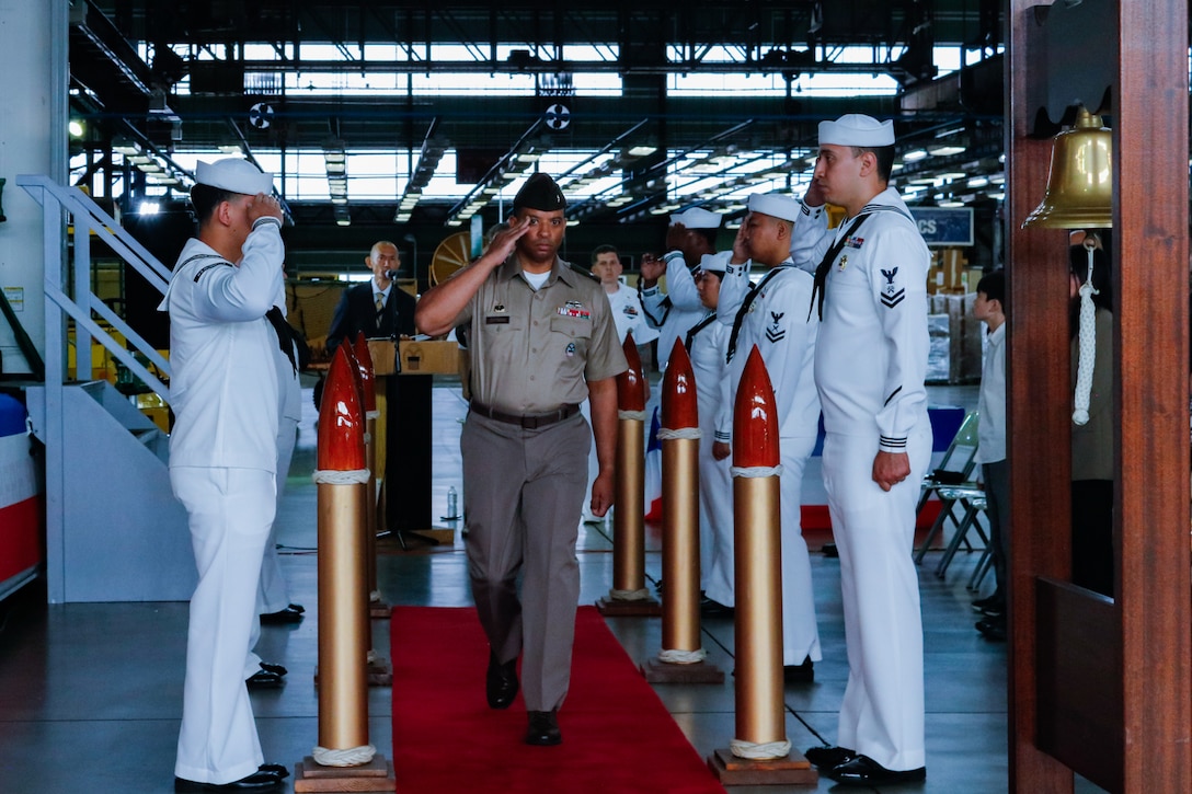 A person dressed in a military uniform walks down an aisle saluting.