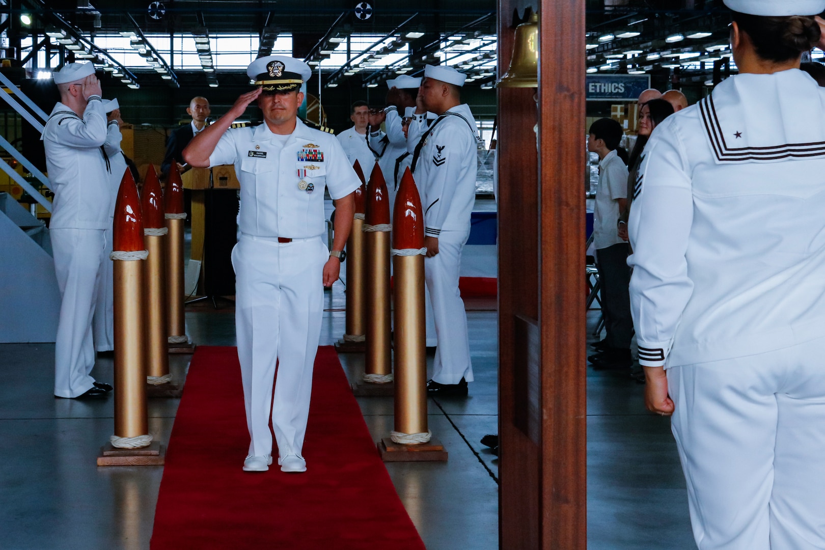 A person dressed in a military uniform walks down an aisle saluting.