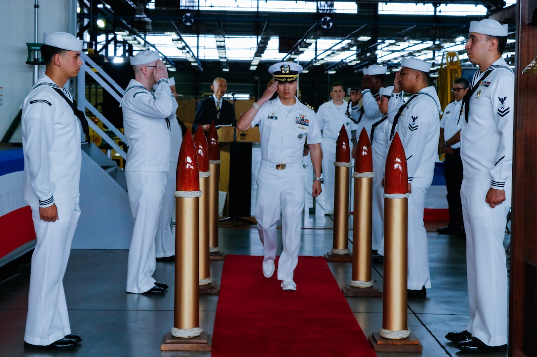 A person dressed in a military uniform walks down an aisle saluting.