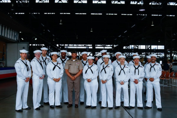 A large group of people wearing military uniforms pose for a group photo inside a large warehouse