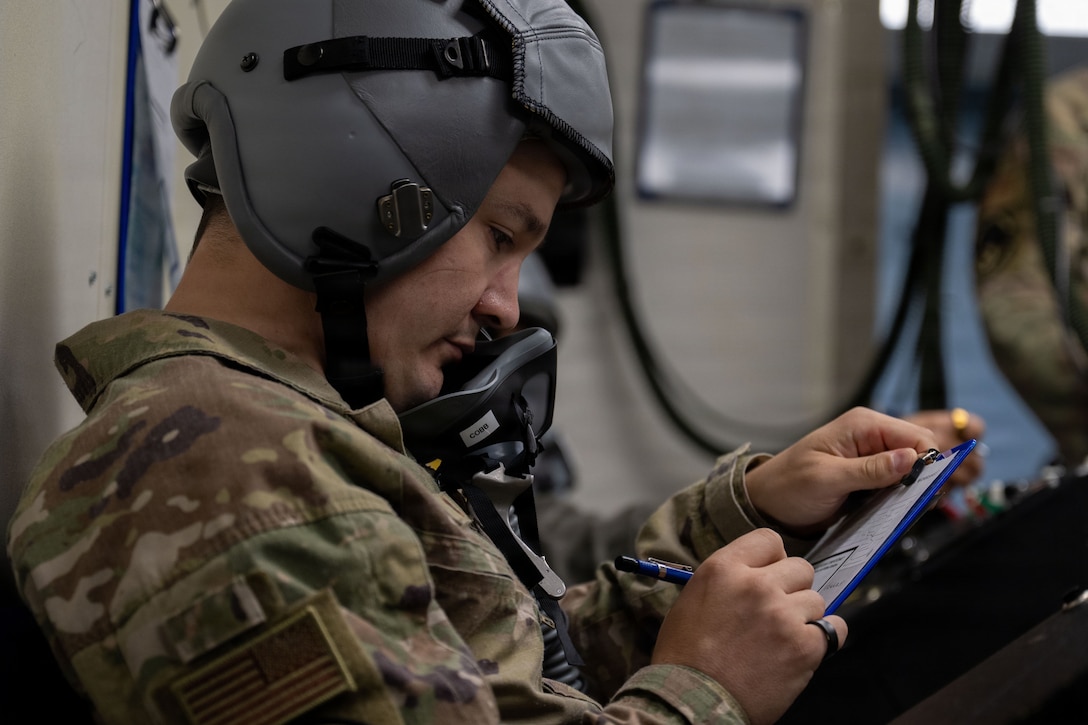 A man in OCPs and a helmet fills out paperwork.