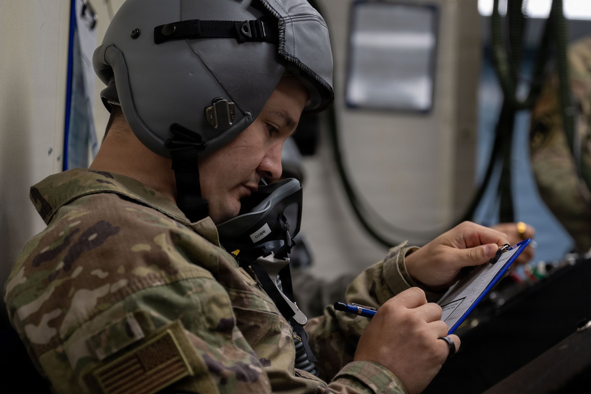 A man in OCPs and a helmet fills out paperwork.