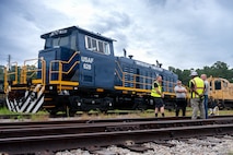 A photo of four men conversing in front of a locomotive.