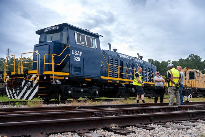 A photo of four men conversing in front of a locomotive.