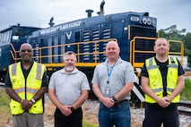 A photo of four men standing in front of a locomotive.