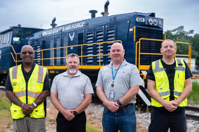 A photo of four men standing in front of a locomotive.