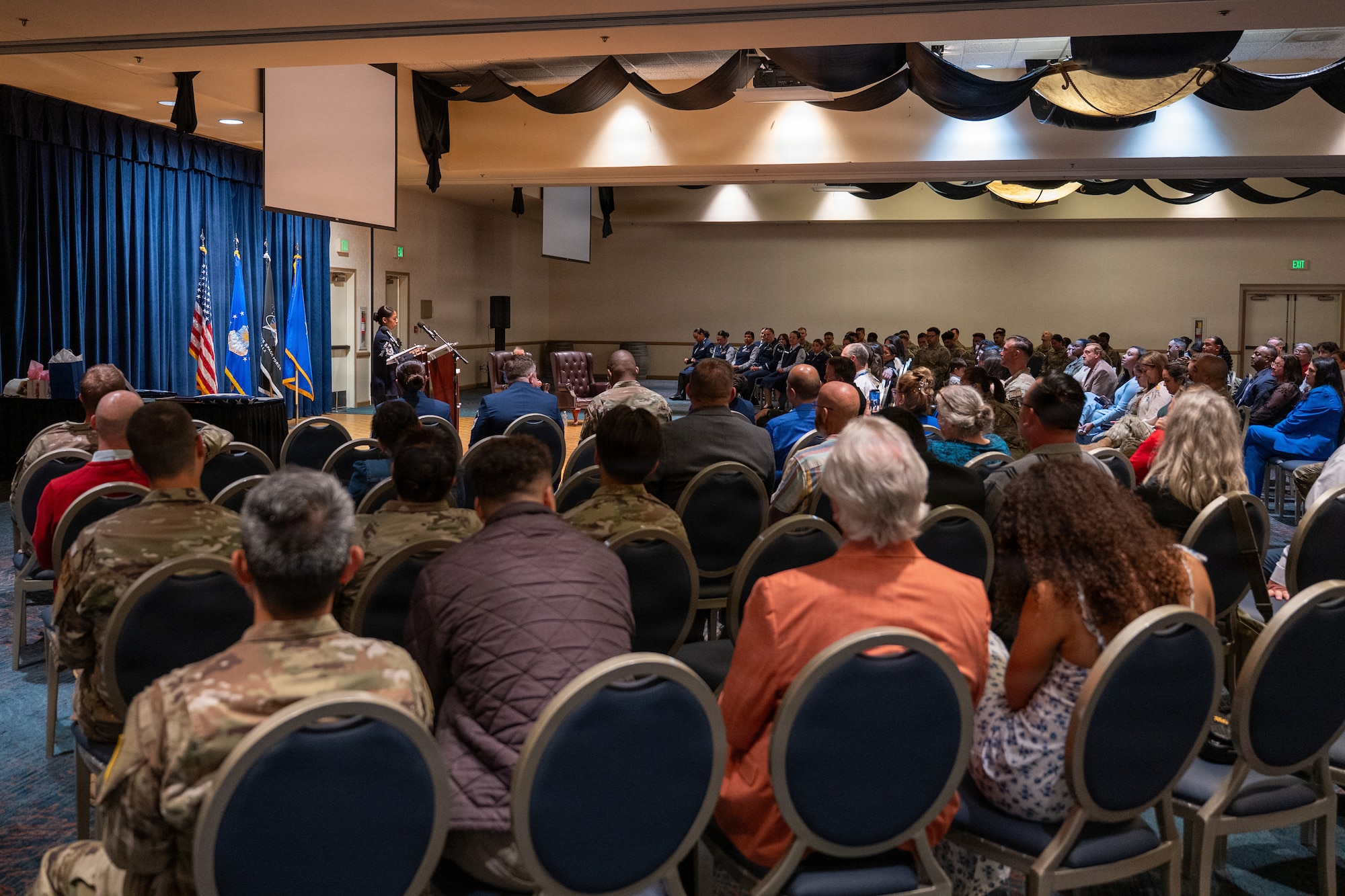 A crowd of people sit and listen to a speaker behind a podium