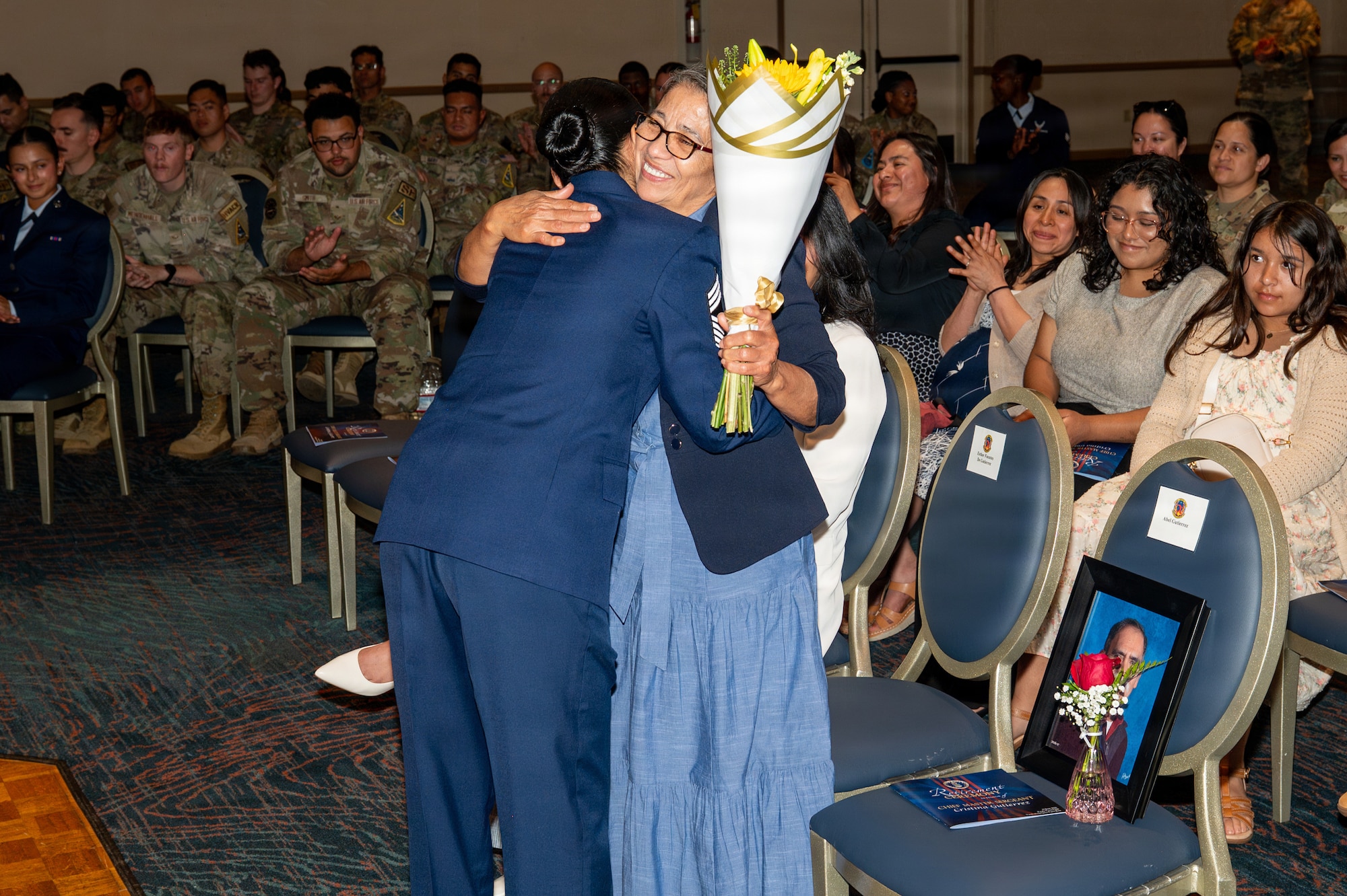 Two people embrace as one holds flowers