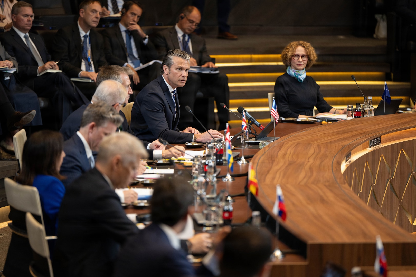 Secretary of War Pete Hegseth speaks while sitting at a curved table with other officials.