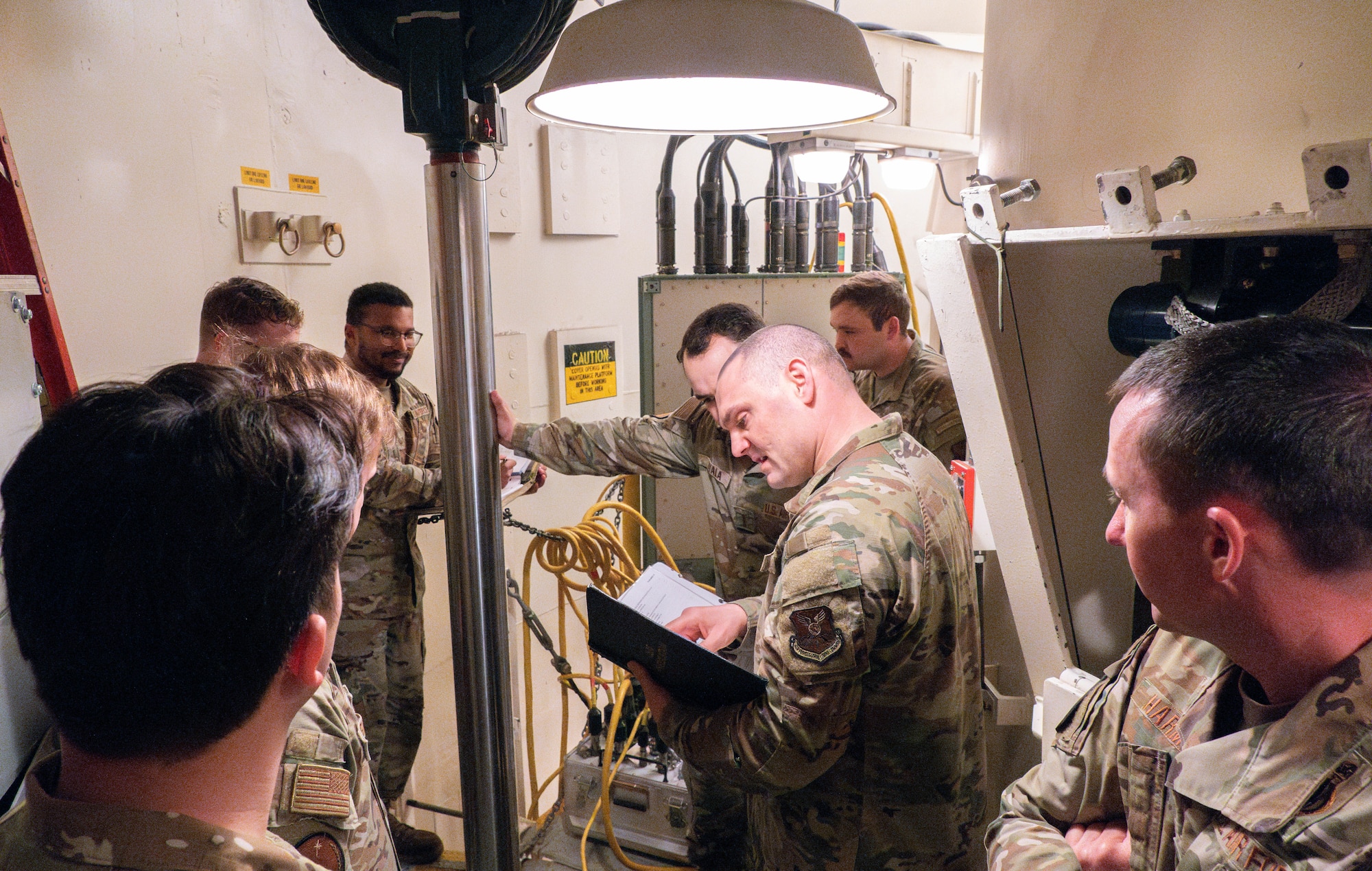 A group of men in uniform stand around a piece of equipment consulting a binder