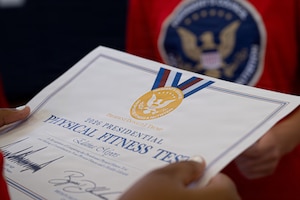A youth center member holds a 2026 Presidential Physical Fitness Test certificate at MacDill Air Force Base, Florida, June 12, 2026.